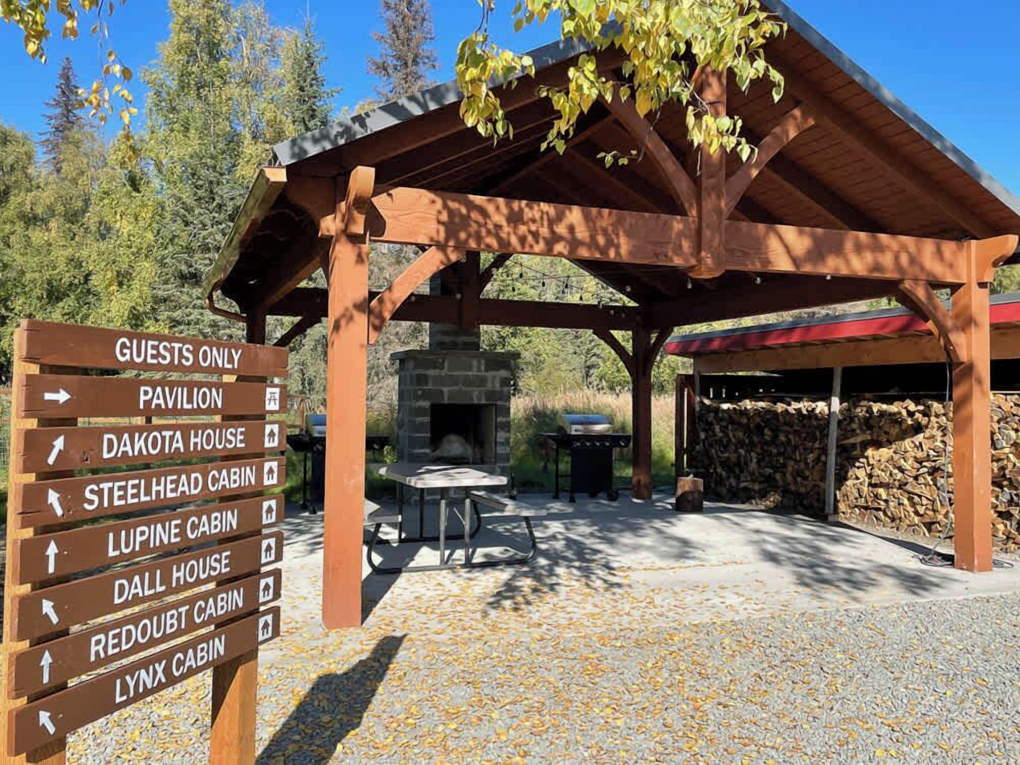 A wooden pavilion with a stone fireplace and a signpost indicating various cabins and a pavilion.