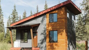 A modern cabin with a wooden exterior and a metal roof, surrounded by trees. - Redoubt cabin @ Keystone Kozy (Soldotna)