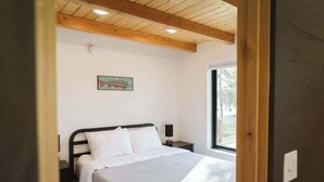 A bedroom with a bed, a nightstand, a wall-mounted light, and a window. - Redoubt cabin @ Keystone Kozy (Soldotna)