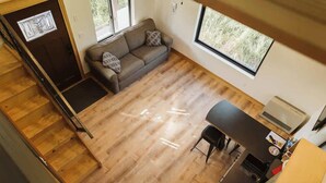 A spacious room with a wooden floor, a sofa, a dining table, and a kitchen area. - Redoubt cabin @ Keystone Kozy (Soldotna)