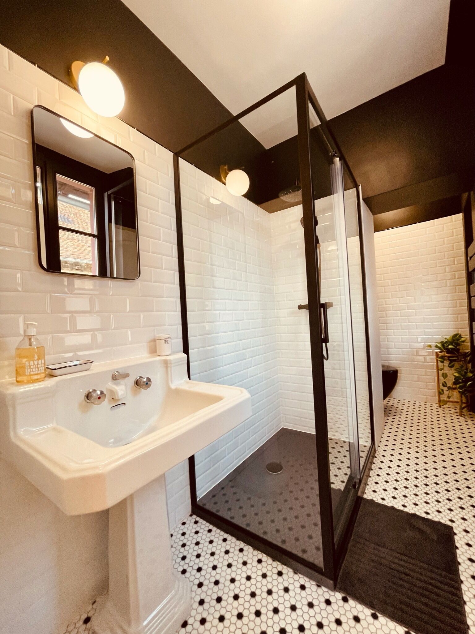 A modern bathroom with a white sink, glass shower enclosure, and a black and white patterned floor.