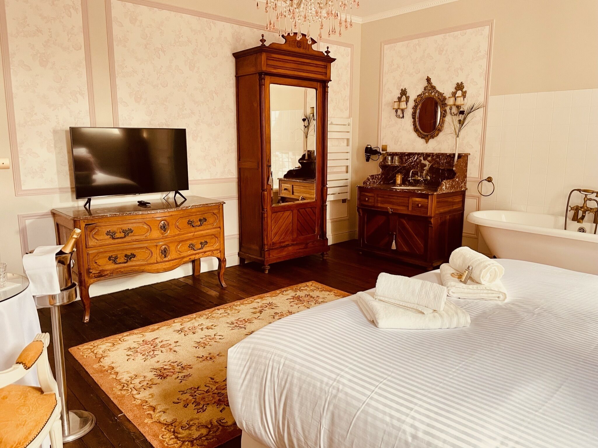 Ein Hotelzimmer mit einem großen Bett, einem Holzschrank, einem Fernseher, einem Schminktisch mit Spiegel und einer Badewanne.