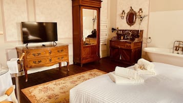 Een hotelkamer met een groot bed, een houten dressoir, een televisie, een kaptafel met spiegel en een bad.