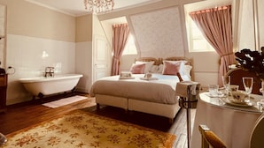 Un dormitorio con cama, un candelabro, un baño con bañera y un comedor con mesa preparada para el té.