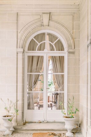 A white arched doorway with a glass panel, flanked by two white urns with plants. - Château du Prieuré - Évecquemont  (Évecquemont)