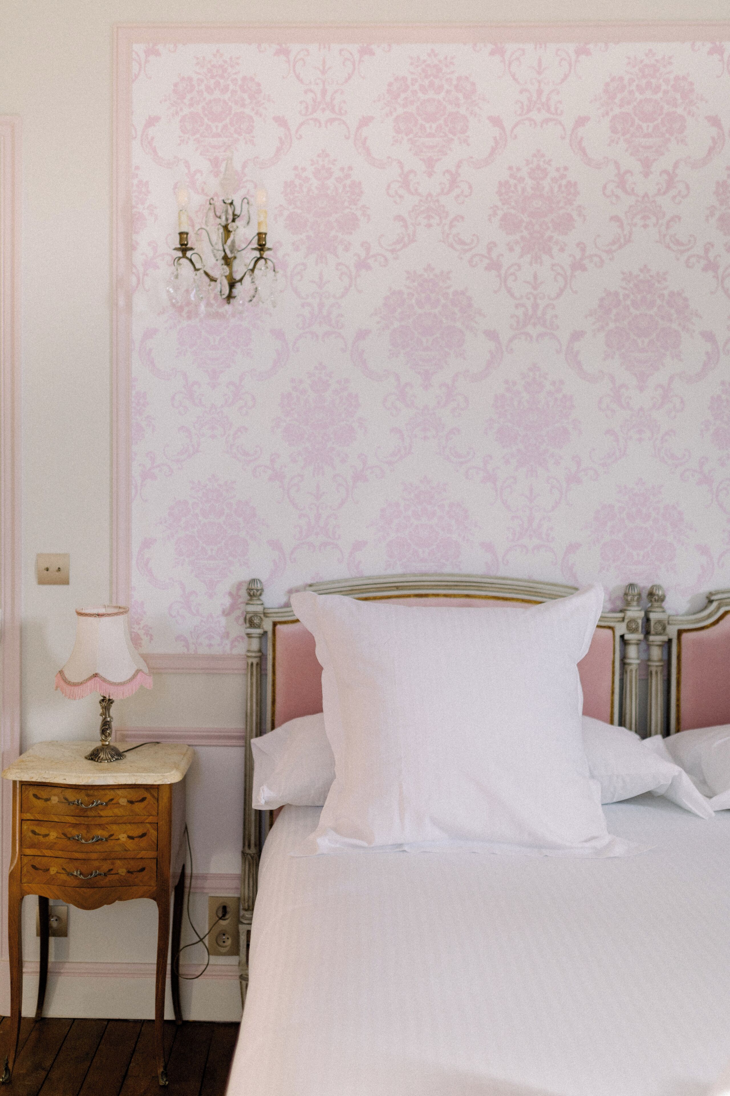Ein Schlafzimmer mit einem Bett, einem Nachttisch, einer Lampe und einer Wand mit floralem Muster.