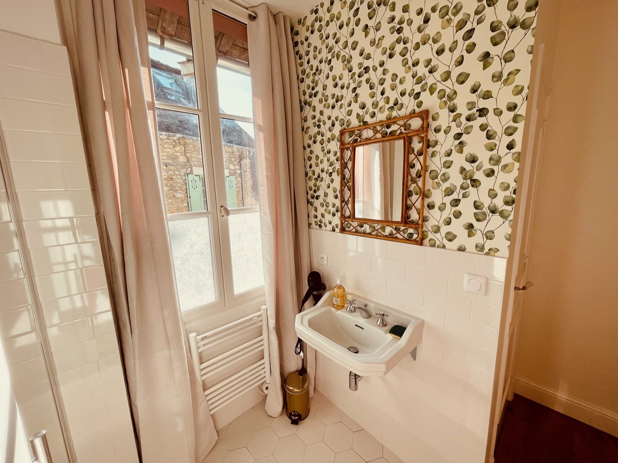 Un bagno con un lavandino bianco, uno specchio e una finestra con tende.