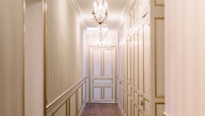 Un pasillo con suelo de madera, paredes blancas y un candelabro.