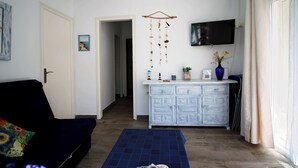 Une pièce avec un canapé noir, un tapis bleu à motifs, une commode blanche, un téléviseur et un élément décoratif suspendu.