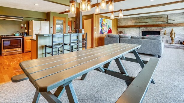 A modern kitchen with a built-in oven, a dining area with a wooden table and benches, and a living room with a gray sofa and fireplace. - Mountain Haus: 4 br, a/c, firepit, free ski shuttle! (Stowe)