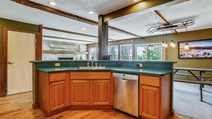 A modern kitchen with wooden cabinets, a stainless steel dishwasher, and a green countertop. - Mountain Haus: 4 br, a/c, firepit, free ski shuttle! (Stowe)