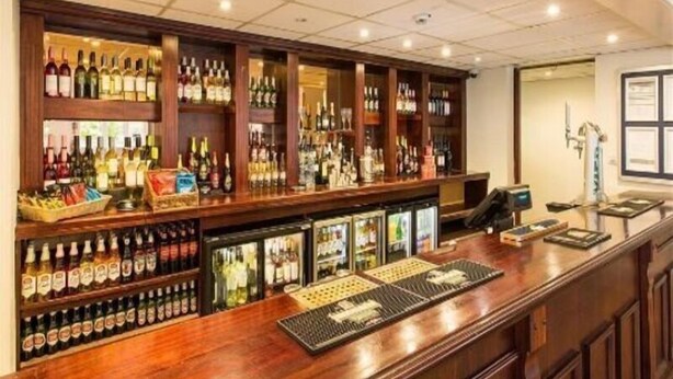 Zona de bar amb estantes plenes de botelles i gots diversos, una caixa registradora i un monitor informàtic.