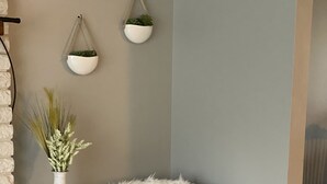 Un coin de pièce avec un fauteuil gris, un plaid blanc moelleux, un vase contenant des plantes séchées et un pot suspendu.