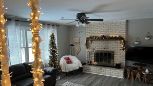 Un salon chaleureux avec une cheminée, un canapé en cuir noir, un fauteuil moelleux blanc et un sapin de Noël.