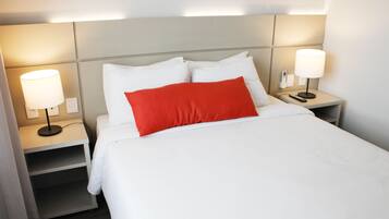 Een hotelkamer met een opgemaakt bed, twee nachtkastjes met lampen en een hoofdbord met ingebouwde verlichting.