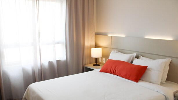 A hotel room with a bed, a nightstand, a lamp, and a window with curtains.