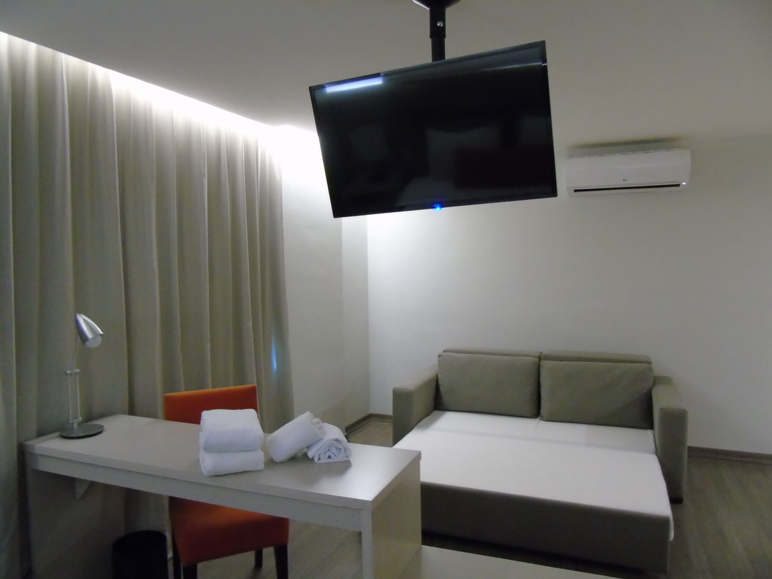 Une chambre d’hôtel équipée d’un lit, d’un bureau, d’une chaise, d’un téléviseur fixé au mur et d’un appareil de climatisation.