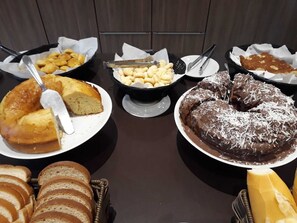 A buffet table with various food items including a cake, bread, and a chocolate dessert. - Samba Três Rios (Tres Rios)