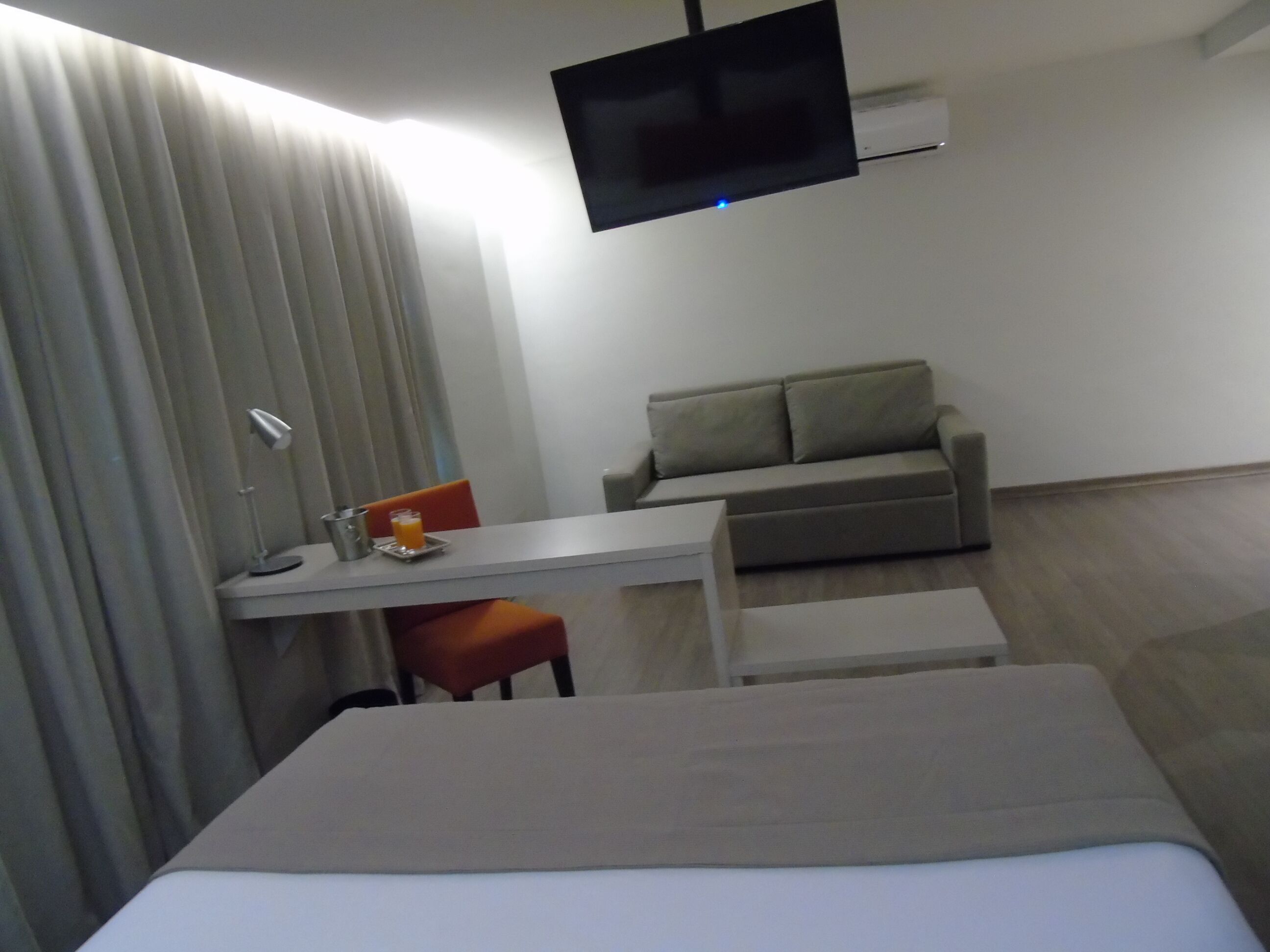Una camera d'albergo con un letto, una scrivania, una sedia, un divano e una TV a schermo piatto fissata al muro.