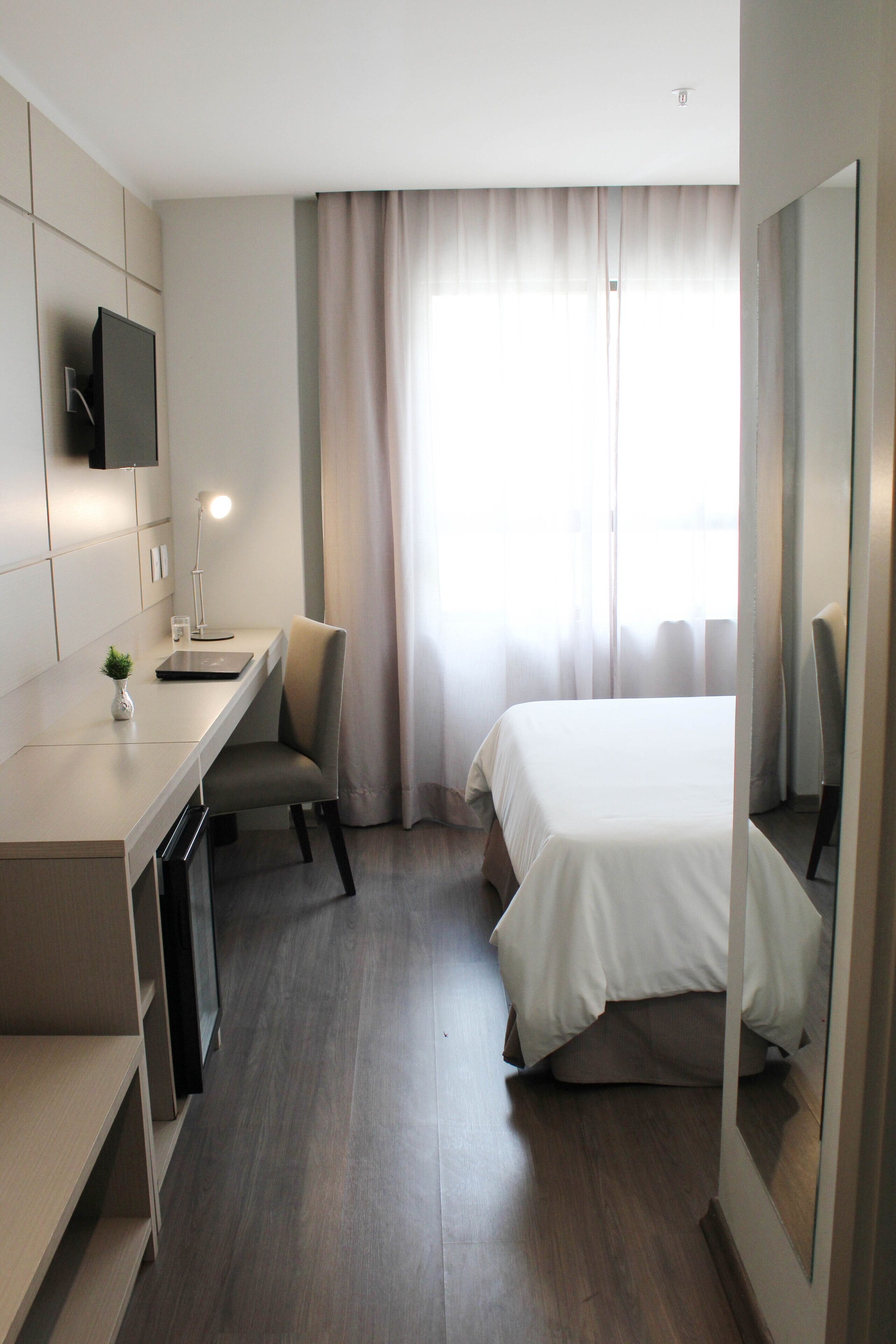 A modern hotel room with a bed, desk, chair, and a flat-screen TV mounted on the wall.