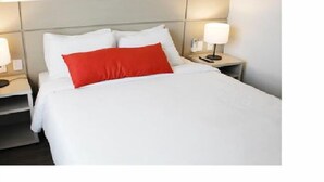A hotel room with a bed, white bedding, a red accent pillow, and bedside lamps.