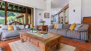 A spacious living area with a wooden coffee table, two sofas, and a large window offering a view of greenery outside. - Amazing home for 10 people. "La Casa del Laurel" (Tepoztlán)