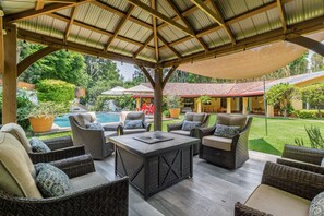 Un espacio de estar al aire libre con techo, mobiliario de mimbre y una piscina al fondo.