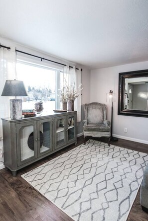 A living room with a grey cabinet, a chair, a patterned rug, and a window with curtains.
