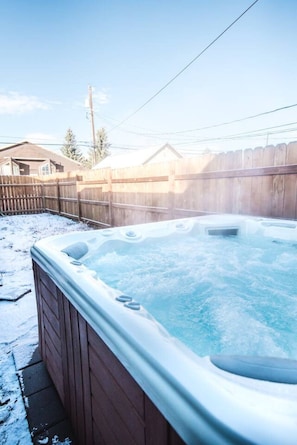 Un bain à remous dans un jardin, avec une clôture en bois et une maison en arrière-plan.