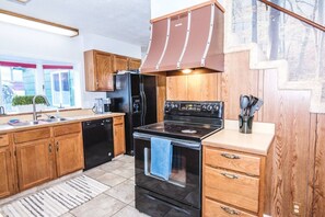 A kitchen with wooden cabinets, a black stove, a dishwasher, and a refrigerator.