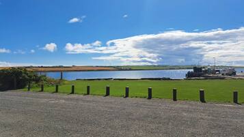 A gravel path leading to a grassy area with a body of water and industrial structures in the background.
