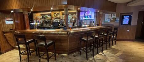 Un espace bar doté d’un comptoir en bois, de plusieurs tabourets et d’un écran de télévision.