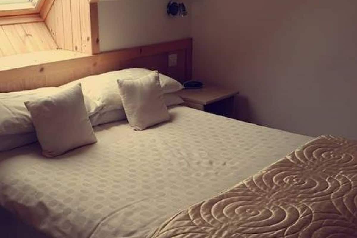 A bedroom with a bed, pillows, a bedside table, and a skylight.