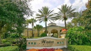 Une enseigne indiquant l’emplacement du club-house de Windsor Hills, entouré de jardins aménagés et de palmiers.