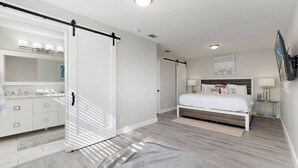 Ein modernes Schlafzimmer mit einer Schiebetür zum Kleiderschrank, einem Bett mit Kopfteil, Nachttischen und einem großen Spiegel.