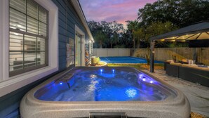 Ein Whirlpool mit blauer Beleuchtung, eine überdachte Terrasse und ein Tennisplatz im Hintergrund.