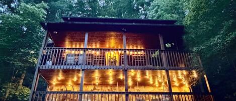 Una cabaña de madera con varios niveles, un balcón y luces colgantes.