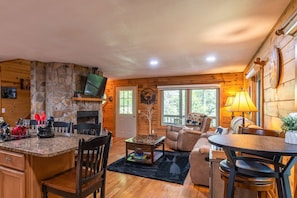 Cozy cabin-style interior with a stone fireplace, comfortable seating area, and large window.