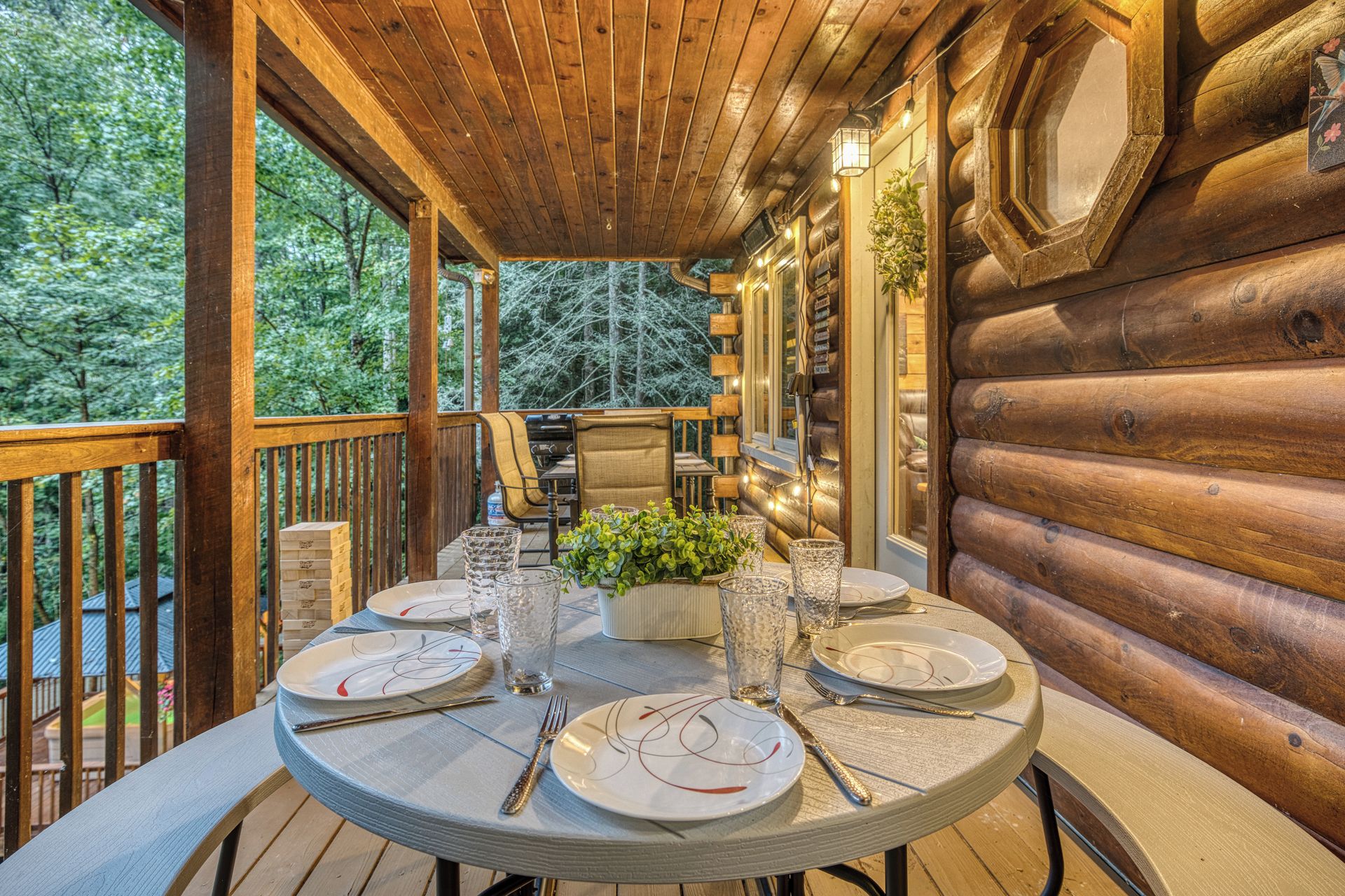 Una terraza de madera con una mesa lista para comer, rodeada de paredes de cabaña de troncos.