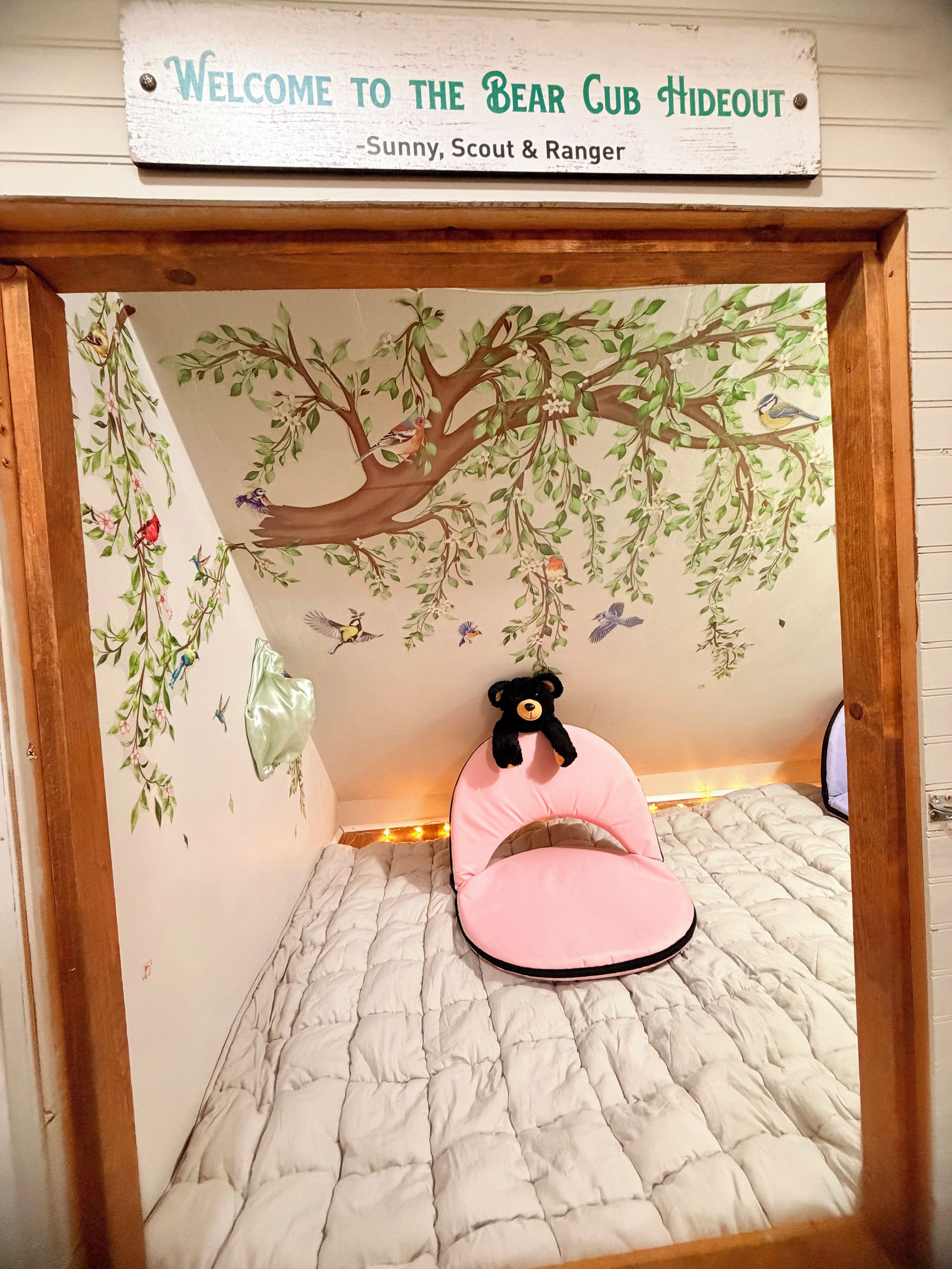 Un refugio acogedor con un mural de árboles, un oso de peluche y una silla rosa.