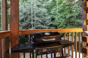 Ein Grill auf einer Holzterrasse mit Wald im Hintergrund.