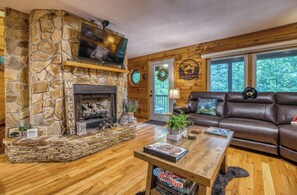 A cozy living room with a stone fireplace, leather sofa, and a television mounted above it.