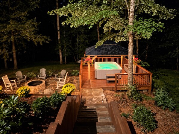 A hot tub on a wooden deck surrounded by chairs and a fire pit.