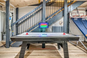 Ein Shuffleboard-Tisch in einem Raum mit einer Holztreppe und einem Basketballkorb.