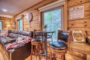 A cabin interior with a leather sofa, a wooden dining table, and a bar stool.
