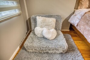 A corner room with a grey furry chair, a small white pillow, and a grey furry rug.