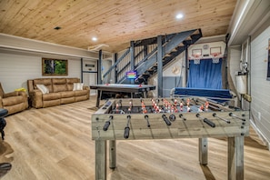 Een kamer met een tafelvoetbaltafel, een bank, een trap en een basketbalring.