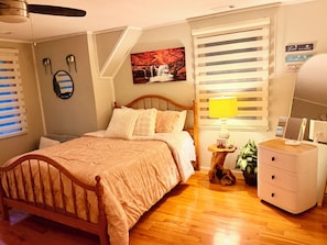 A bedroom with a wooden bed, a bedside lamp, a dresser, and a wall-mounted mirror.