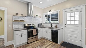 A modern kitchen with white cabinets, a stainless steel range hood, a built-in oven, a dishwasher, and a window above the sink. - Cozy Home Overlooking Manito Park + Free parking! (Spokane)