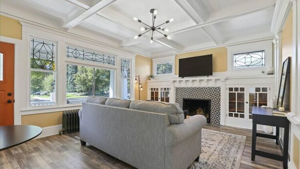 A living room with a gray sectional sofa, a fireplace, and a large window with decorative glass panes. - Cozy Home Overlooking Manito Park + Free parking! (Spokane)